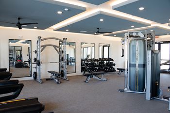 A gym with a variety of equipment including treadmills, weights, and a bench press at The Crest at South Point Apartments, Davenport , GA